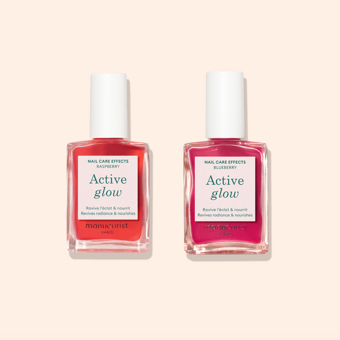 Two bottles of Manucurist Active™ Duo nail care for natural nails—one Raspberry (pink), one Blueberry (deep pink)—are displayed on a light beige background, ideal for gentle nail repair.