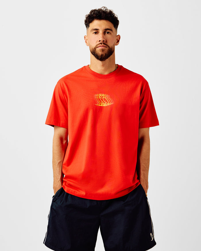 Man wearing red crewneck t-shirt with yellow graphic print on chest, paired with black shorts.