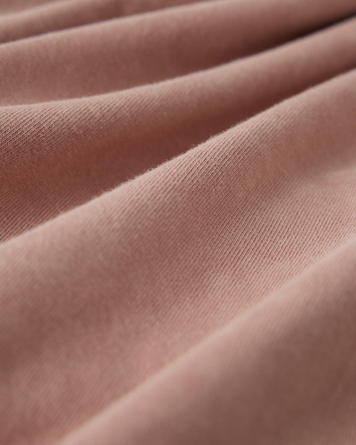 Clay pink ribbed fabric with diagonal folds and texture detail.