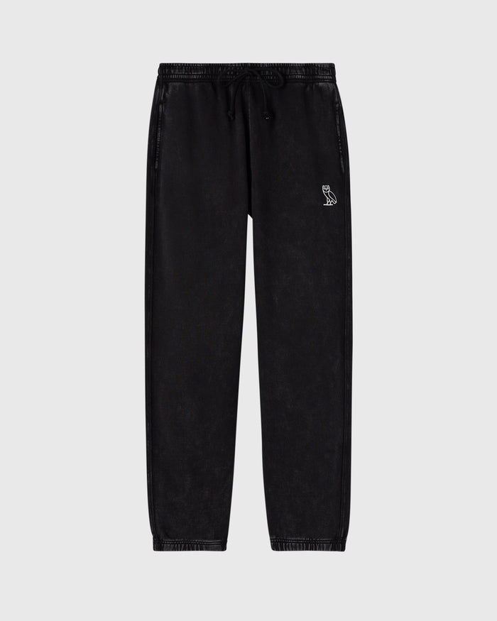 Black garment-dyed sweatpants with drawstring waist and small logo emblem on thigh.