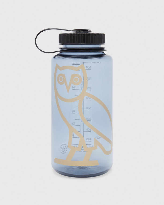 Light blue plastic water bottle with black screw-top lid, attached carry loop, and tan owl graphic with measurement markings.