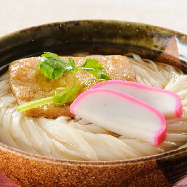 Bowl of noodles with fish cake and radish slices in a brown ceramic bowl.