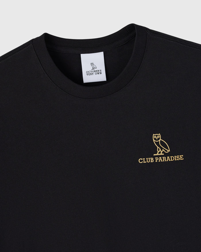 Black t-shirt with gold owl and "Club Paradise" text on chest, white brand label at neckline.