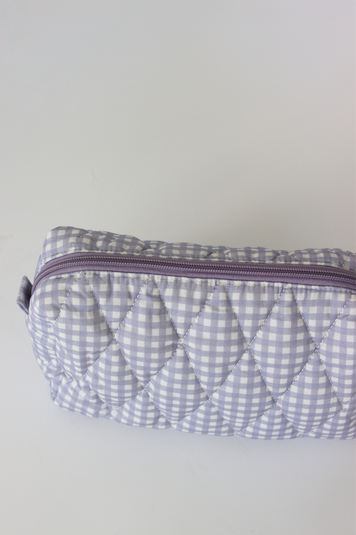 A quilted cosmetic pouch with a light purple and white gingham pattern, featuring a matching purple zipper, shown on a plain light gray background.