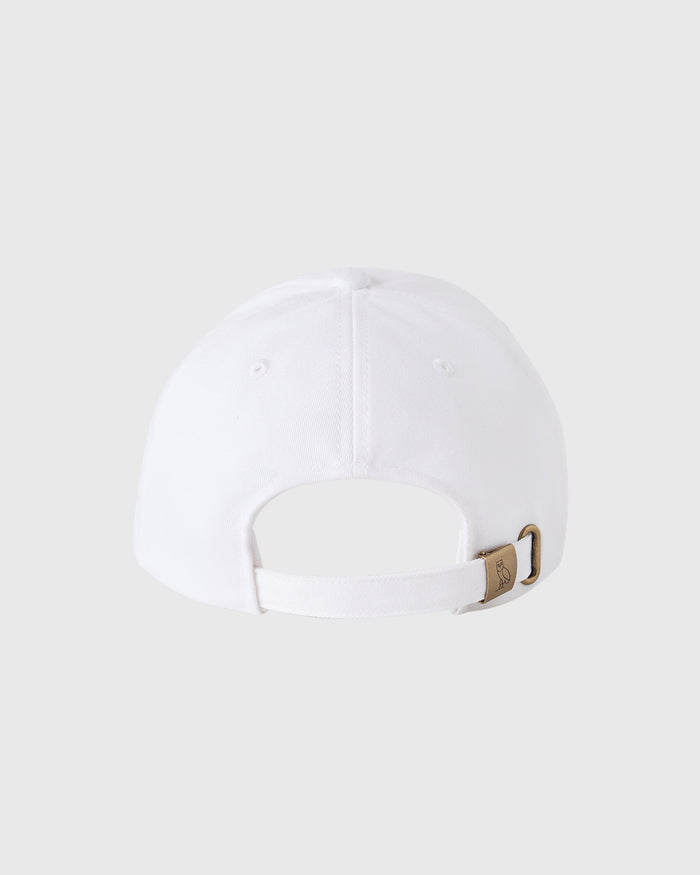 White baseball cap with pom pom on crown and adjustable strap with brown buckle closure at back.