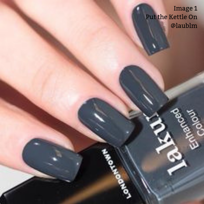 Close-up of a hand with dark gray polished nails holding two bottles of LONDONTOWN's vegan cruelty-free nail polish. Text reads "Image 1 Put the Kettle On @laublm.