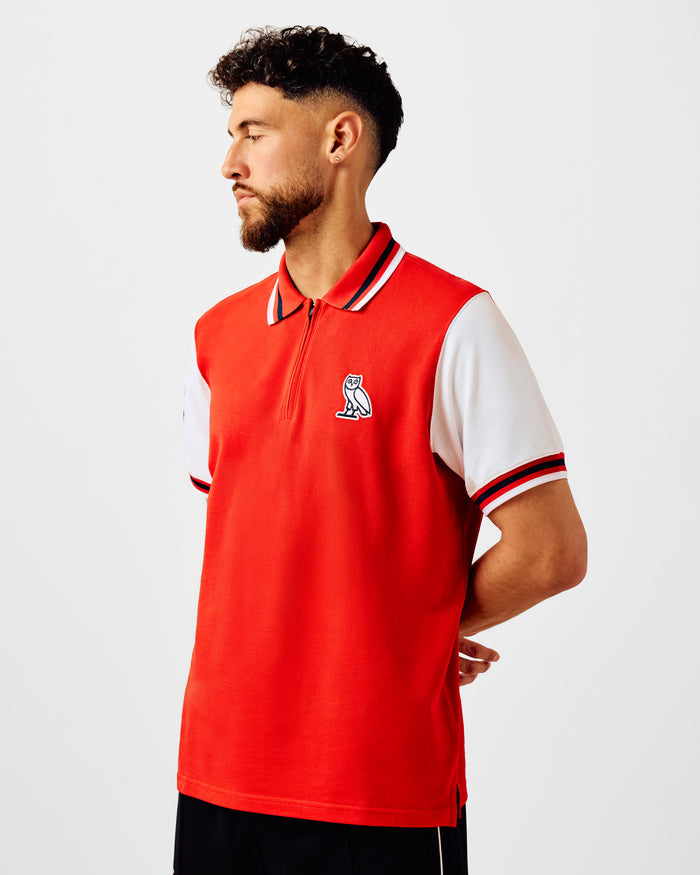 Man wearing red and white short-sleeve polo with quarter-zip, striped collar and owl logo.