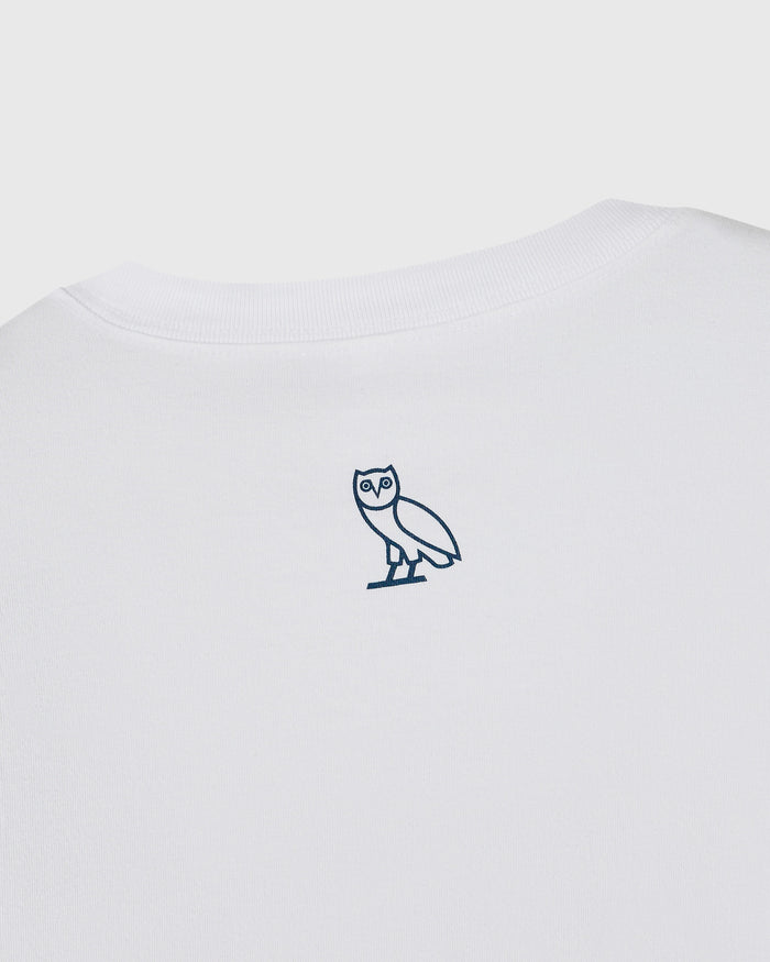 White t-shirt with small navy owl emblem on chest.