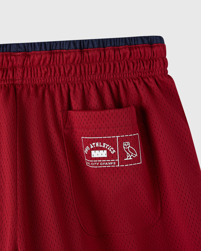 Deep red mesh shorts with navy waistband, front pocket with embroidered athletics logo, reversible design visible.