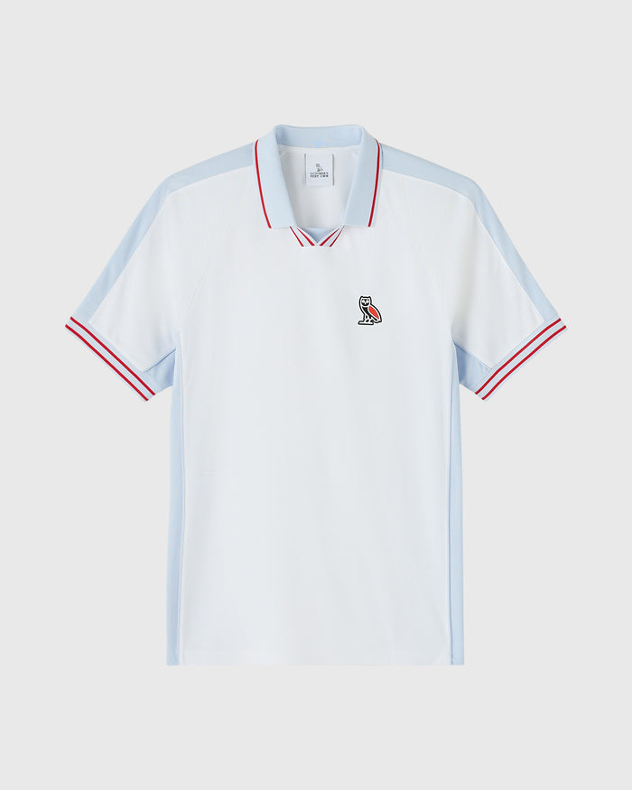 White piqué polo shirt with light blue side panels, red and white striped collar and cuffs, and small embroidered owl logo on