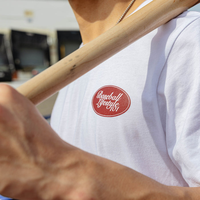 Close-up of red Baseball Lifestyle 101 oval chest graphic on white youth tee, wooden bat resting across chest.