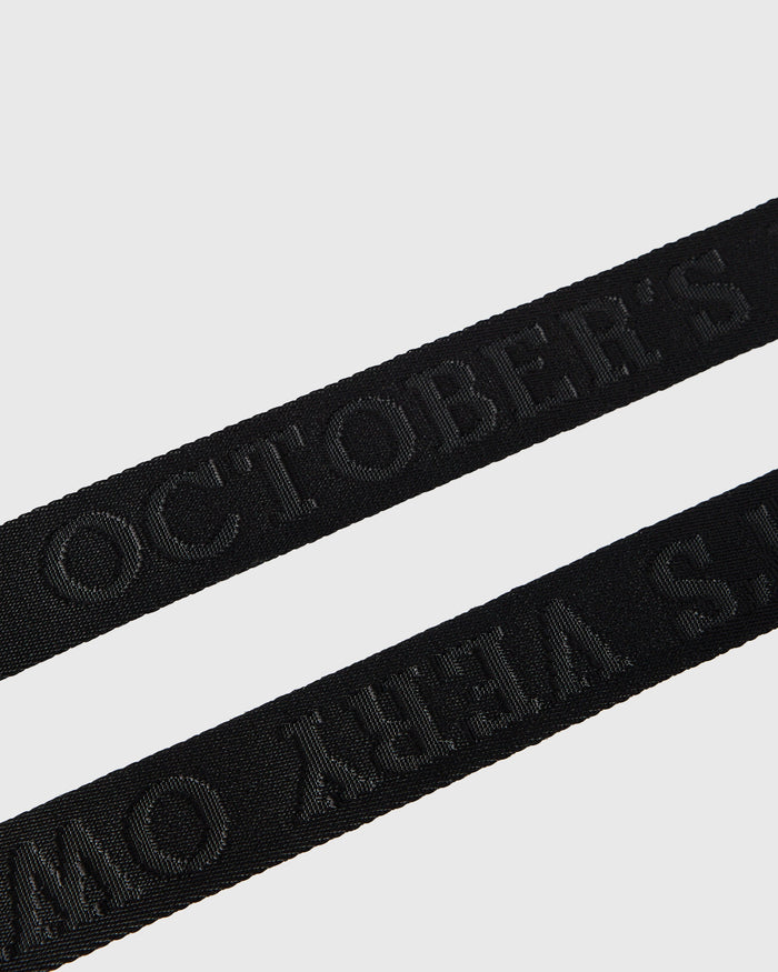 Black webbed belt with woven text pattern displayed diagonally on neutral background.