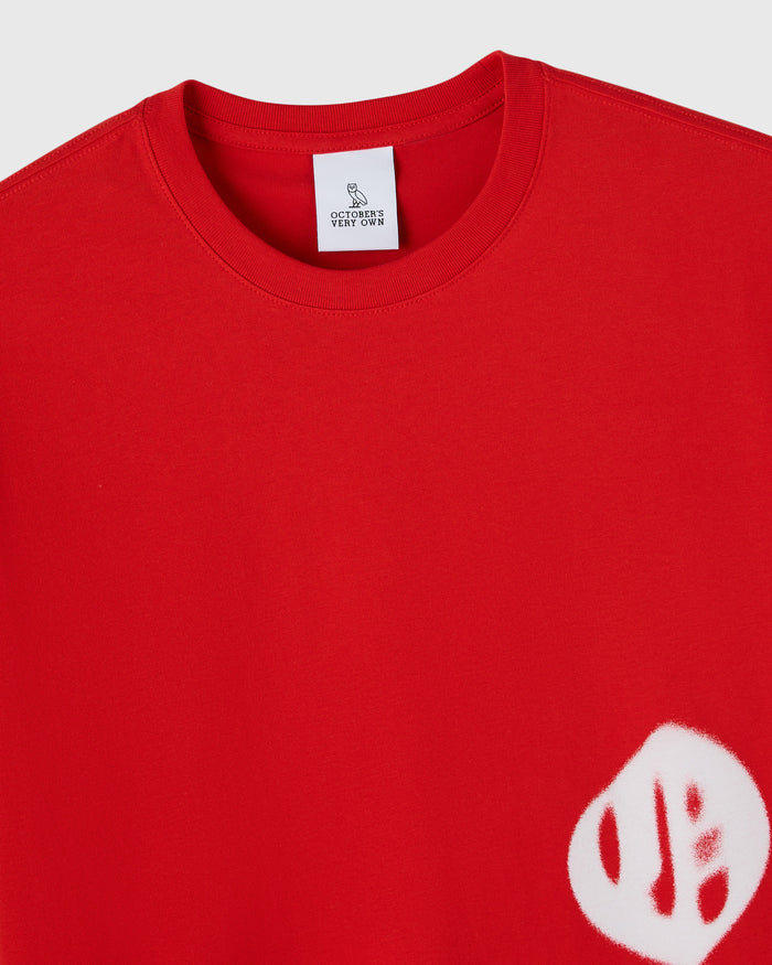 Red crewneck t-shirt with white airbrushed graphic on lower right chest and brand label at neckline.
