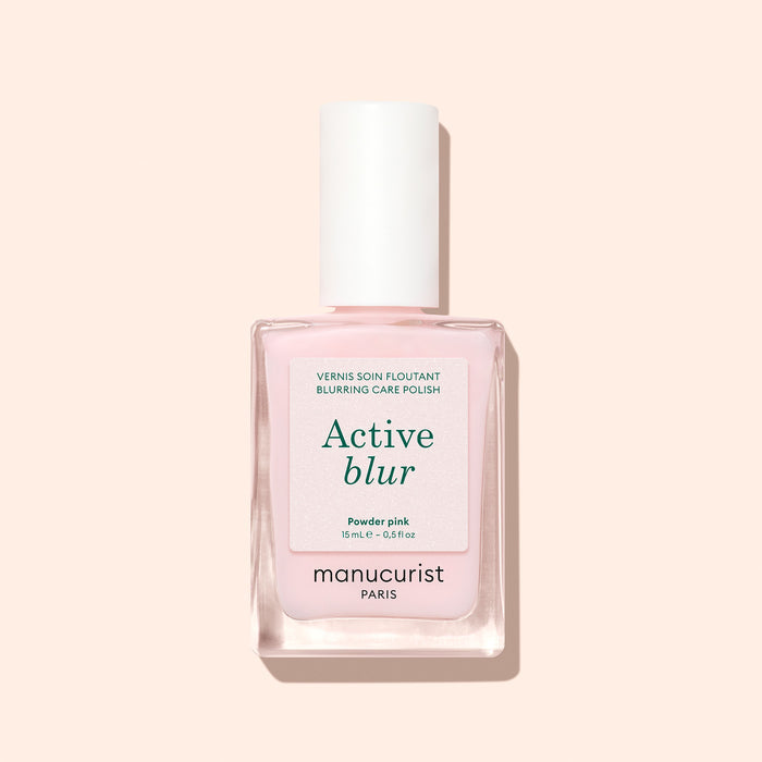 A bottle of Manucurist Active™ Blur nail polish in powder pink, showcasing a flawless matte finish and topped with a white cap adorned with a minimalist label, displayed against a light beige background.