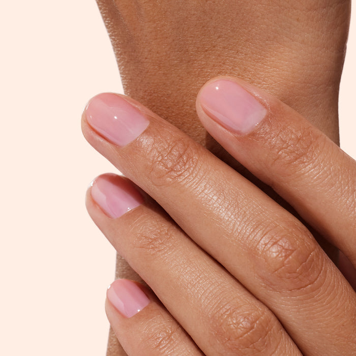 A close-up of a hand with neatly manicured nails painted in a light pink, glossy polish—resting gently on another part of the same hand against a neutral background—showcases the naturally healthy, beautiful results achieved with Manucurist Active™ Glow Blueberry nail care.