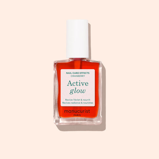 A bottle of Manucurist Active™ Glow Cranberry plant-based nail care polish with a white cap, displayed on a light beige background, provides beautifully tinted glow nails for a naturally radiant look.