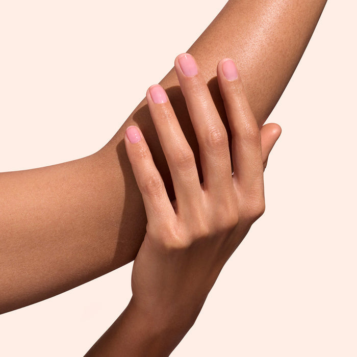A close-up of a hand with neatly manicured, natural-looking nails showcasing a subtle glow from Manucurist’s Active™ Glow Grape, gently resting on a forearm against a light beige background.