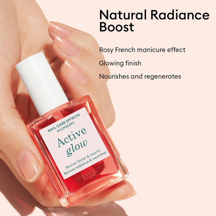 A hand holds a pink bottle of Manucurist Active™ Glow Raspberry nail care polish, with text highlighting its radiant, nourishing, and glowing manicure effects—infused with plant-based ingredients for advanced nail nourishment—on a light pink background.