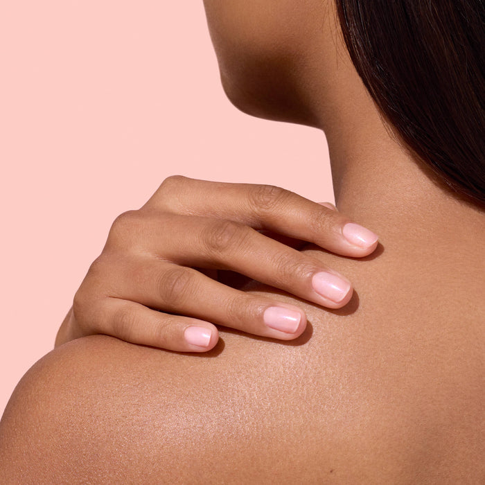 A person with smooth skin touches their bare shoulder with neatly manicured nails painted in Manucurist’s Active™ Plump Pink Glazed, showcasing the benefits of this plant-based nail care against a soft pink background.