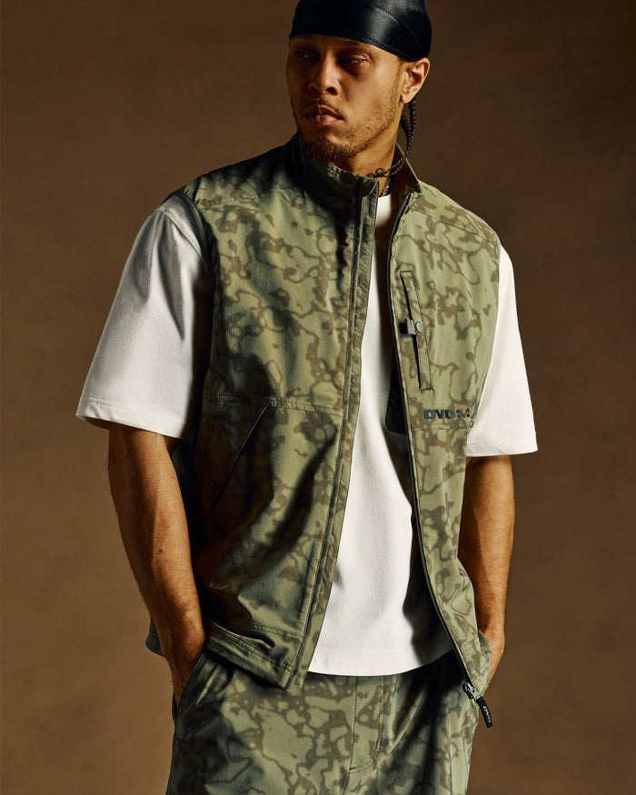 Cream short-sleeve t-shirt worn under a patterned utility vest with multiple pockets.