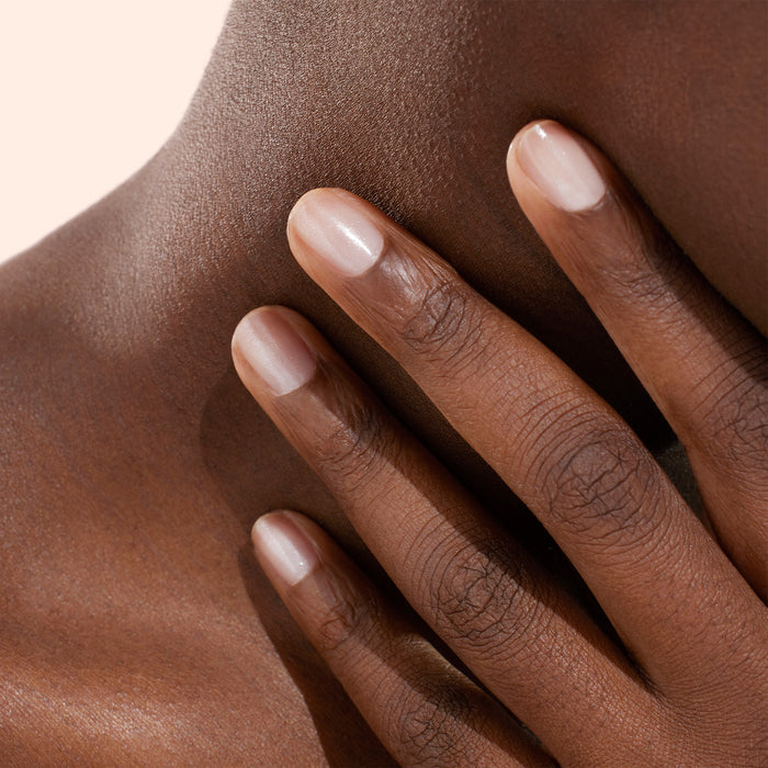 A close-up of a hand with neatly manicured nails, enhanced by Manucurist’s Active™ Shine plant-based nail polish, resting gently on a person’s neck and shoulder, highlighting smooth, dark brown skin.