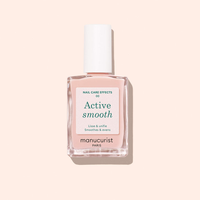 A bottle of Manucurist Active™ Smooth 00 nail treatment, topped with a white cap, sits on a light pink background. The white label features green and black text, highlighting the brand’s dedication to plant-based nails.