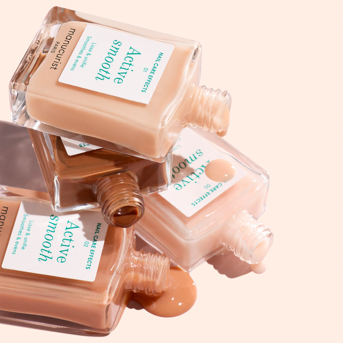 Three open bottles of Manucurist Active™ Smooth 02 nail polish in varying nude shades are stacked and spilling polish onto a light surface, highlighting the ideal fusion of color and nail care for your ultimate nail treatment.