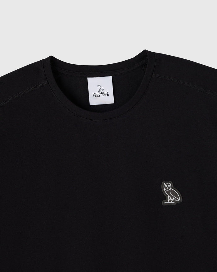 Black crew neck tee with small owl embroidery on chest and brand label at neckline.