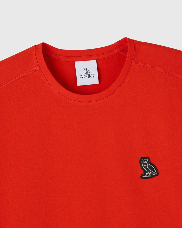 Signal orange crew neck tee with small owl embroidery on chest and brand label at neckline.