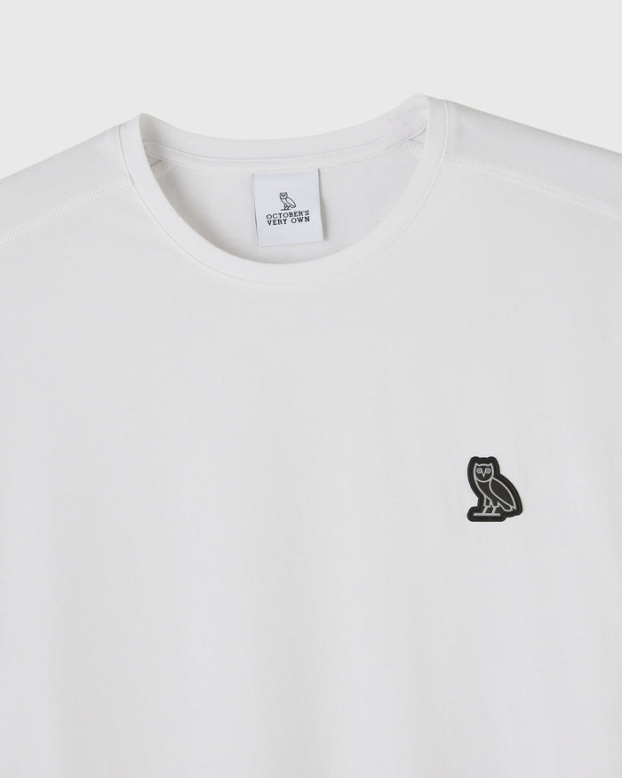 White crewneck t-shirt with small black owl embroidery on chest and brand label at neckline.