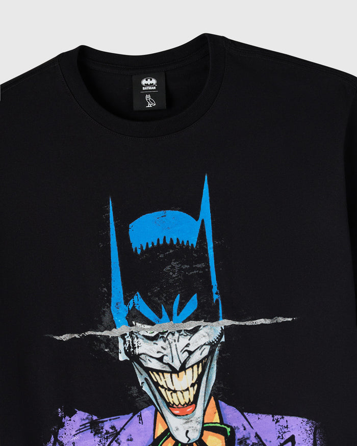 Black crewneck tee with split design showing Batman mask in blue and black on upper half, Joker face with purple jacket on lo