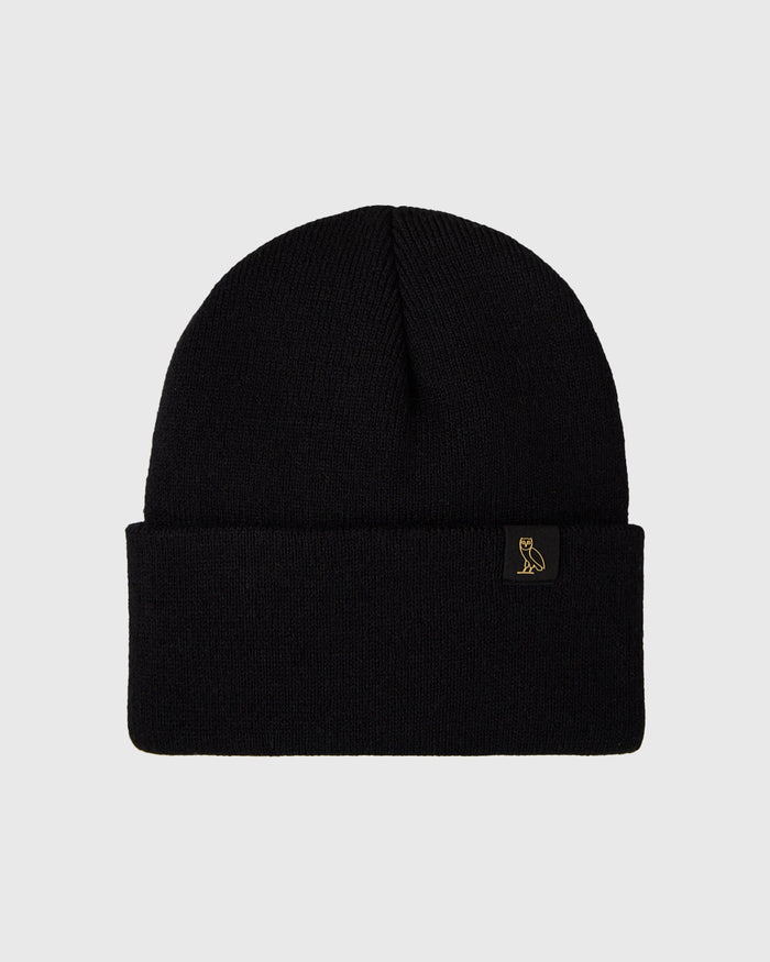 Black ribbed knit beanie with small gold owl emblem on cuff.