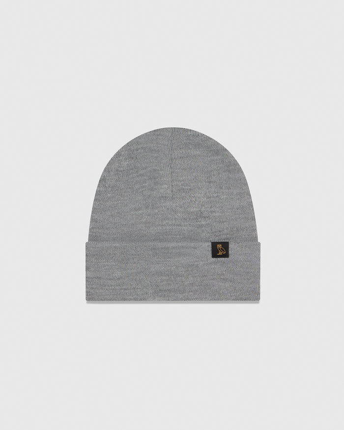 Gray ribbed knit beanie with small black label patch on cuff.