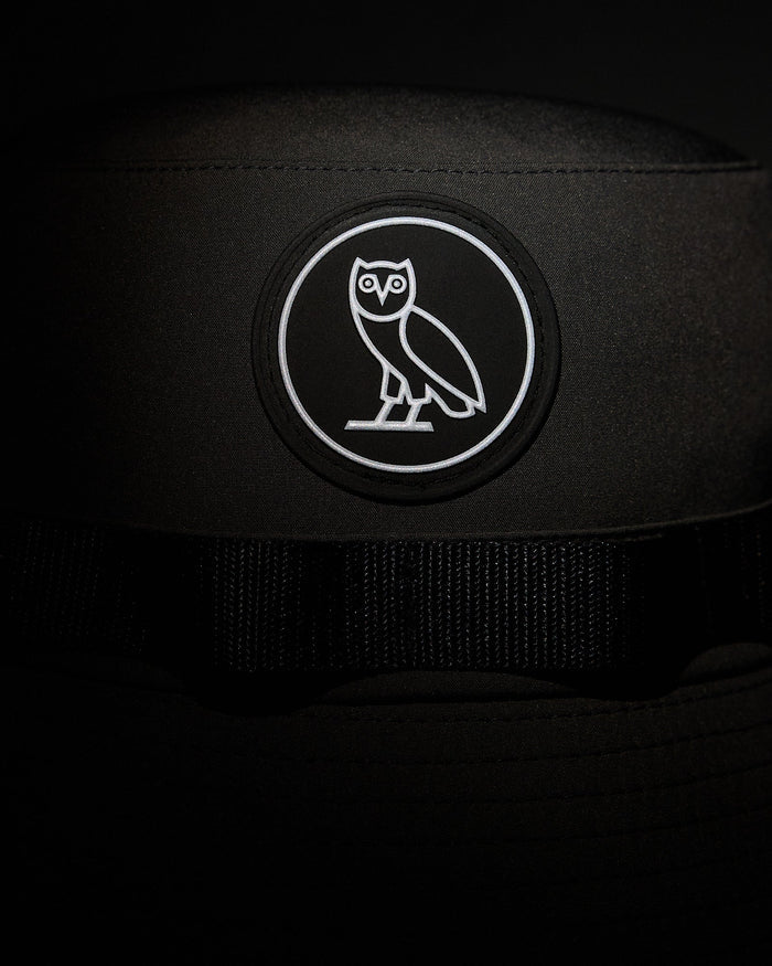 Black boonie hat with white owl emblem patch on front and black webbing strap.