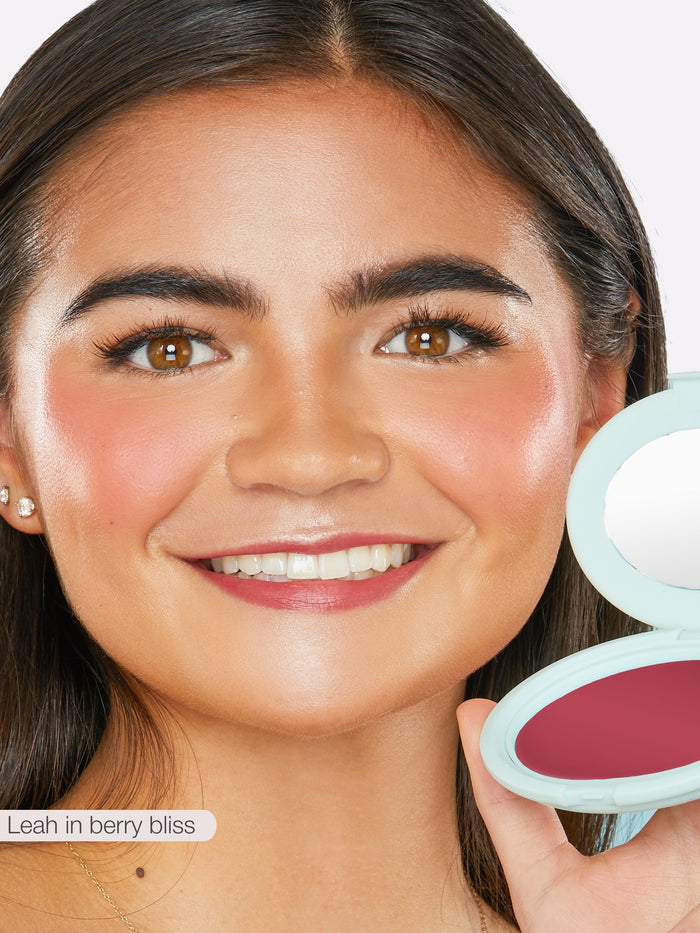 Close-up of a woman's face with blush on, holding a makeup compact.