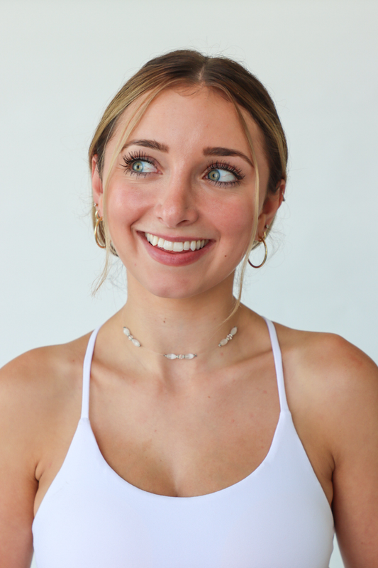 Woman wearing a white tank top against a plain background