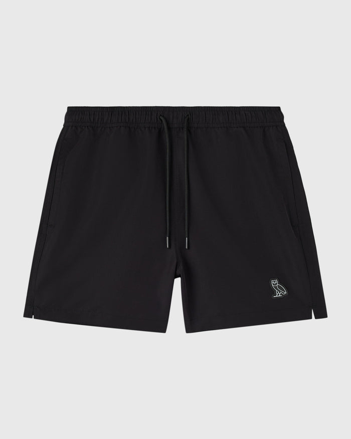 Black swim shorts with elastic waistband, drawstring, side pockets, and small embroidered owl logo on leg.