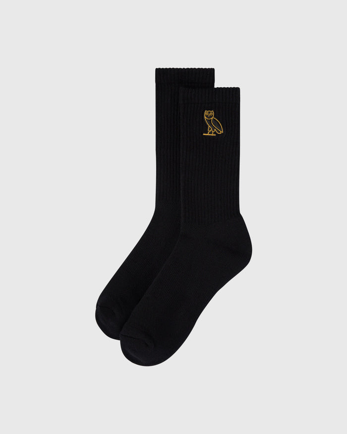 Pair of black ribbed crew socks with small gold owl embroidery on the calf.