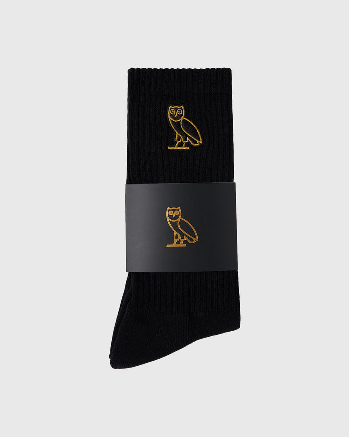 Black ribbed socks with gold owl embroidery, shown with gray fabric band wrapper.