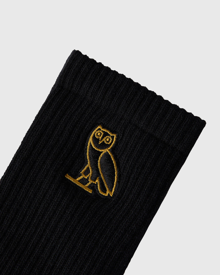 Black ribbed socks with gold embroidered owl design on the calf.