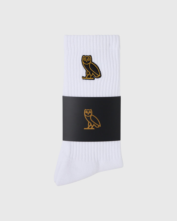 White ribbed socks with gold owl embroidery on upper cuff and black band detail.