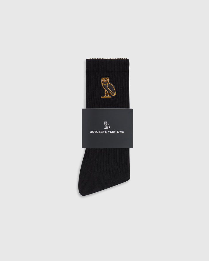 Black ribbed crew socks with gold owl embroidery, displayed with branded packaging band.