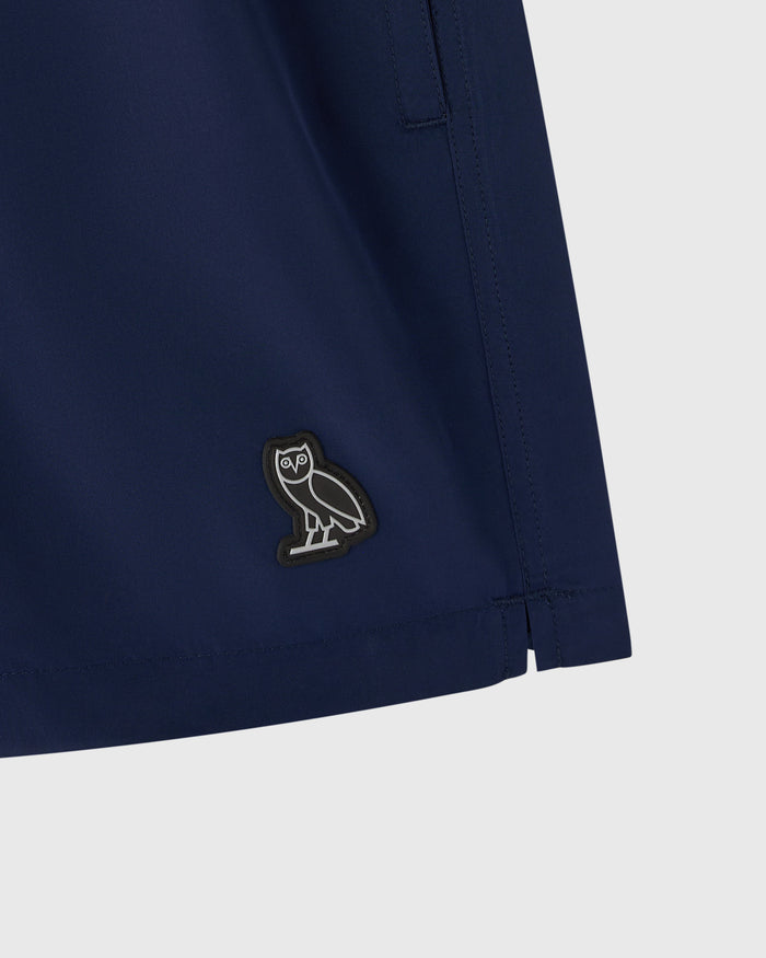 Navy swim short with embroidered owl logo patch and side pocket detail.