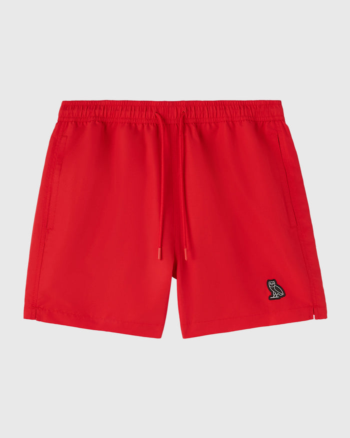 Red swim shorts with drawstring waist, side pockets, and small embroidered logo on the right leg.