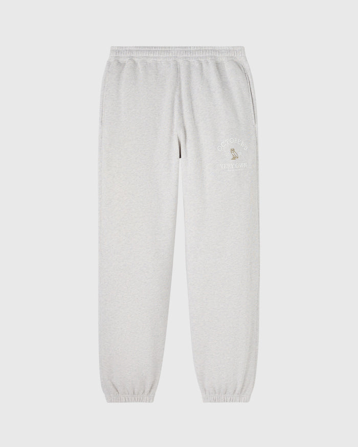 Light gray sweatpants with embroidered text and logo on thigh, elastic waistband and cuffed ankles.