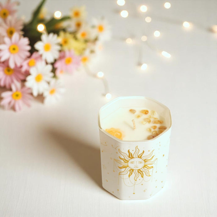 Candle in a decorative holder with sun design, surrounded by flowers and string lights.