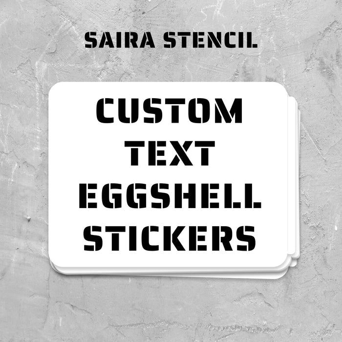 Stack of custom text eggshell stickers with 'Saira Stencil' branding on a textured gray background.