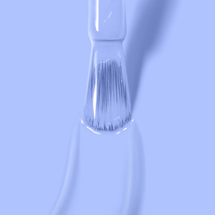 Close-up of a paintbrush applying LONDONTOWN's Dainty Daze vegan cruelty-free periwinkle blue nail polish on a smooth surface, captured in a monochromatic blue tone.