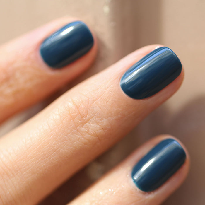 A close-up of a hand with neatly manicured nails painted in Manucurist's Dark Clover gel polish, fingers resting on a smooth beige surface.
