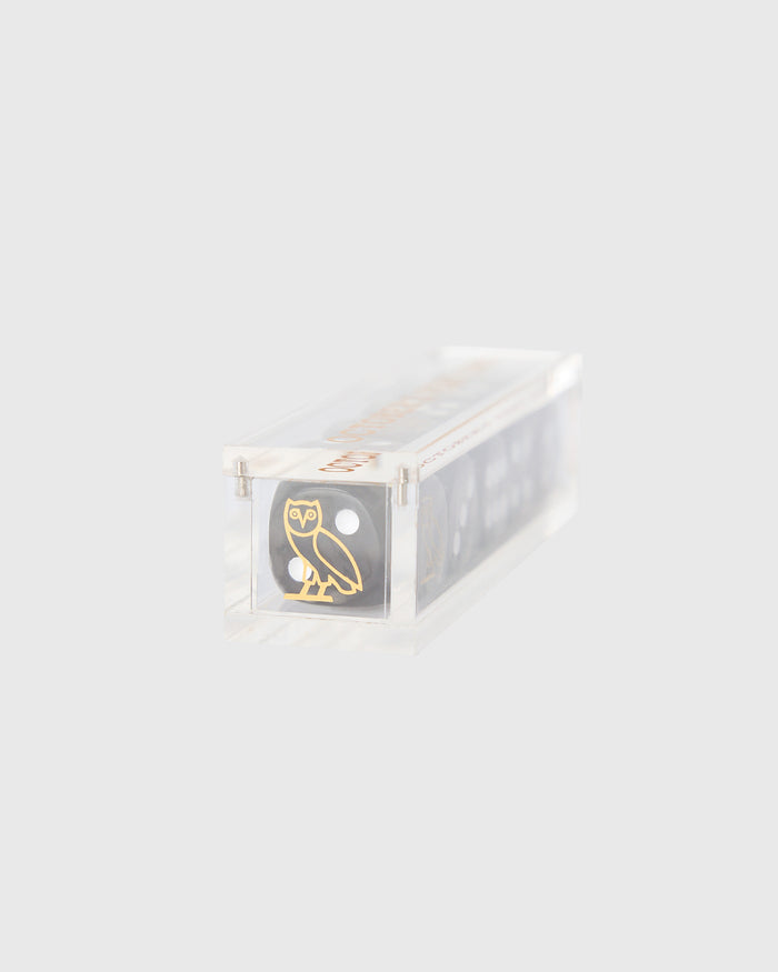 Black dice set in clear plastic container with gold owl logo and numbered sides visible.